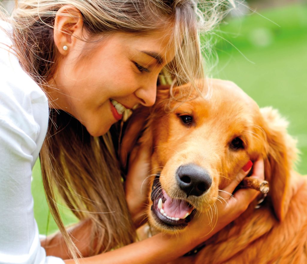 Woman playing outdoors with a golden-brown Golden Retriever, both enjoying an active and joyful moment.